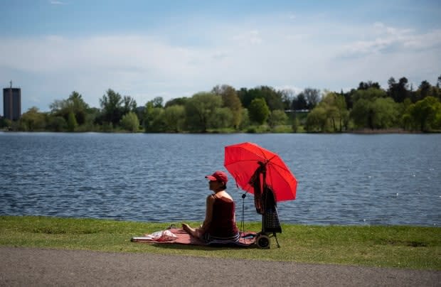 A person rests in dark red sits in the shade of their brighter red umbrella on the edge of Dows Lake in Ottawa May 16, 2021. (Justin Tang/Canadian Press - image credit)