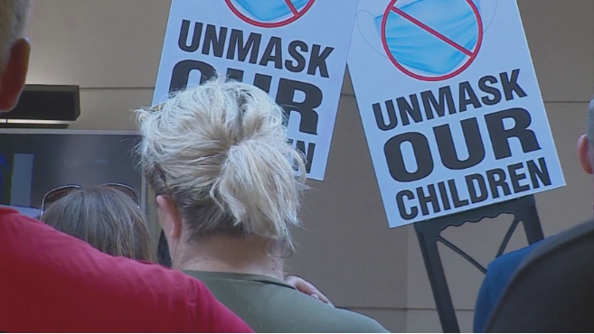 Signs are held protesting a local K-6 mask mandate during the Ottawa County board of commissioners meeting on Tuesday, Aug. 24, 2021, in West Olive, Mich.