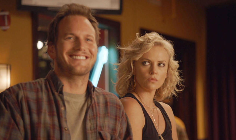 A man in a fleece button-up and undershirt smiles as a blonde woman behind him stares intensely