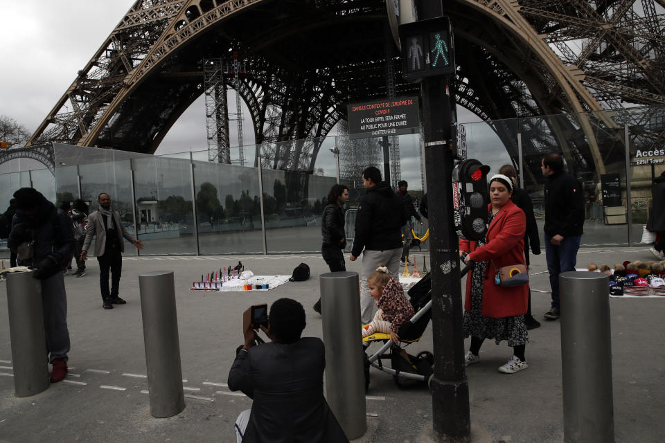 People take picture in front of the Eiffel tower closed after the French government banned all gatherings of over 100 people to limit the spread of the virus COVID-19, in Paris, Saturday, March 14, 2020. For most people, the new coronavirus causes only mild or moderate symptoms. For some it can cause more severe illness, especially in older adults and people with existing health problems. (AP Photo/Christophe Ena)