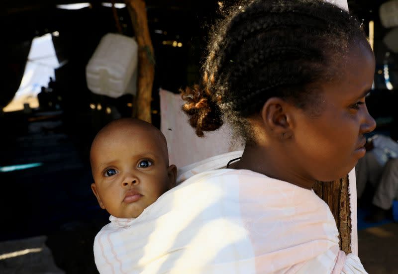 FILE PHOTO: An Ethiopian woman who fled war in Tigray region carries a child on her back as she walks at the Um-Rakoba camp on the Sudan-Ethiopia border in Al-Qadarif state