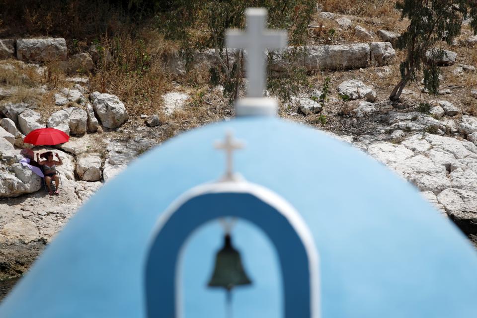 A woman sunbathes on a small beach as a Greek Orthodox chapel is seen the foreground during a warm day in Piraeus, near Athens on Wednesday, May 20, 2020. Public beaches were reopened last weekend amid heatwave temperatures, with strict distancing rules imposed by the government, but crowding did occur on buses from Athens to the nearby coast. Travel to the Greek islands remains broadly restricted due to the coronavirus outbreak. (AP Photo/Thanassis Stavrakis)