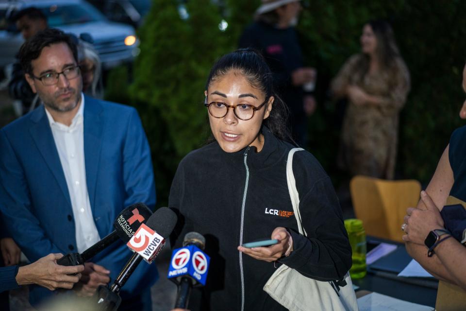 A woman speaks to reporters as microphones are held up toward her face.