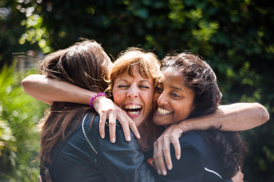 Three women, greeting and hugging outdoors.