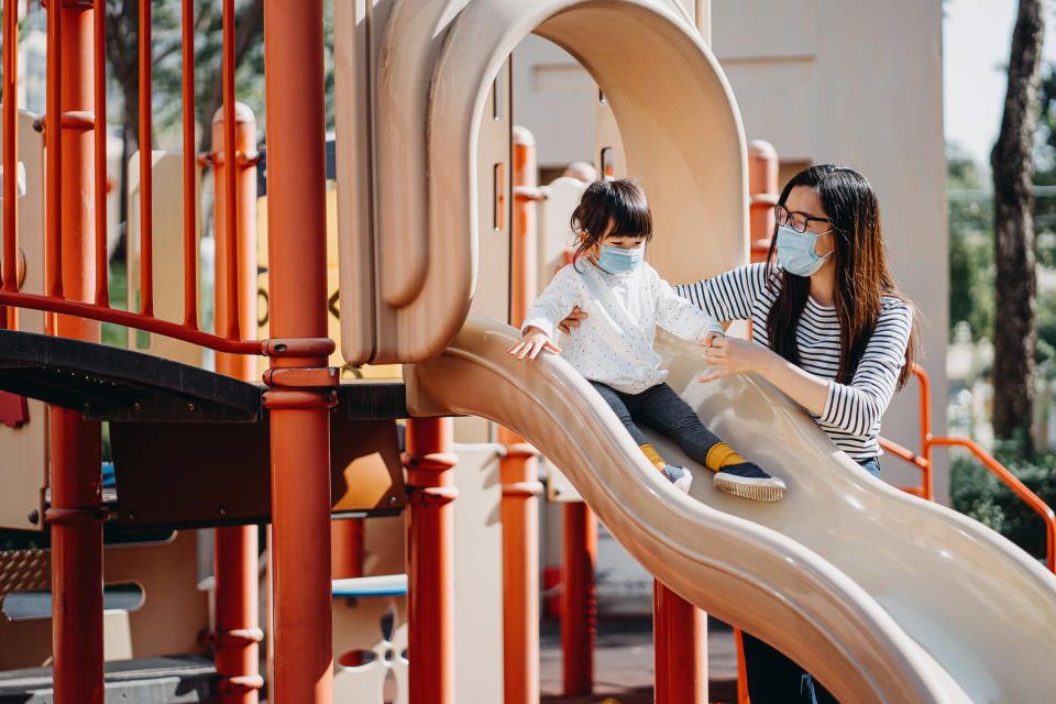 child and parent wearing surgical masks at playground slide