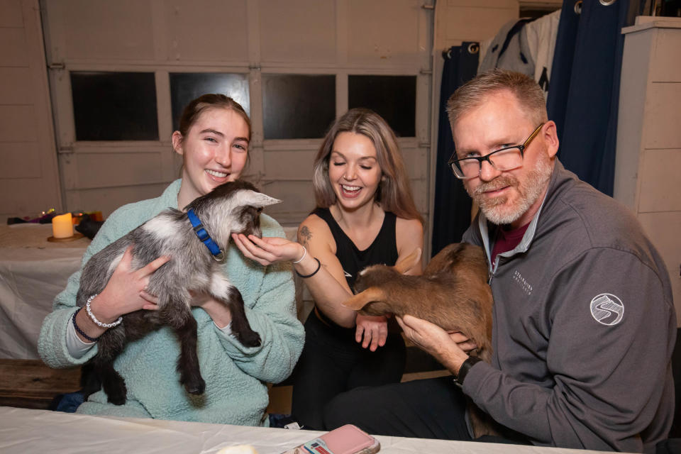 Julia and Jamie Neefe of Concord hold the baby goats with yoga instructor Jessica Lescrinier (center) at the Wine-yasa Goat Yoga night at Legacy Lane Farm in Stratham.