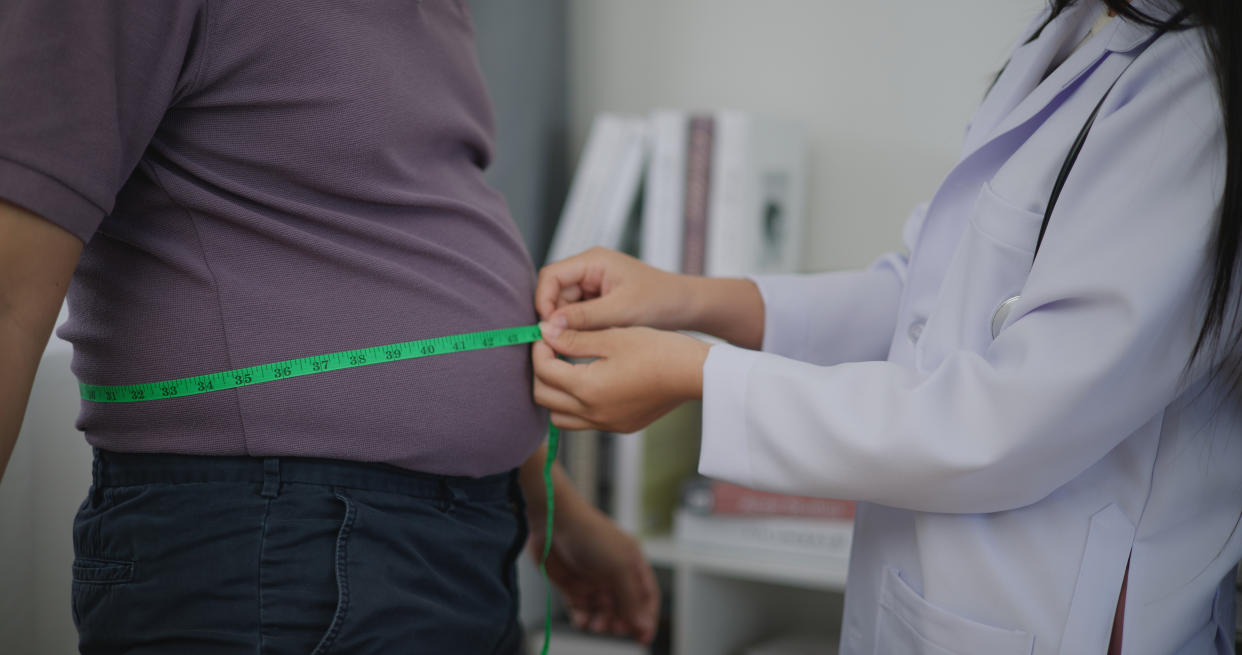 Female Nutritionist measuring waist of overweight man in weight loss clinic during giving consultation to patient with healthy and diet weight loss, Right nutrition and diet concept