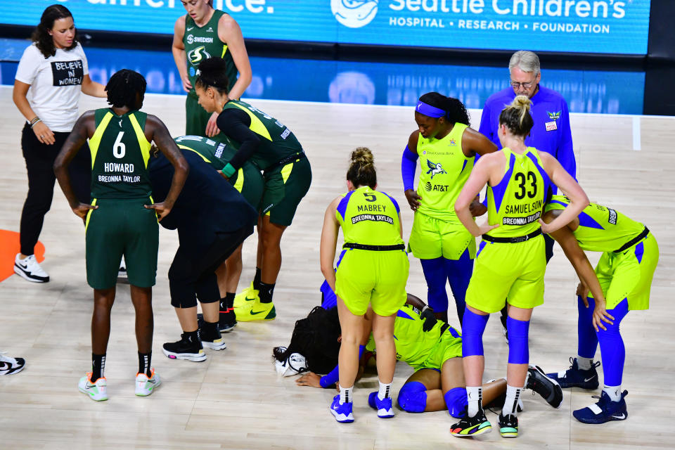 Teammates surround Sue Bird and Satou Sabally on the court.