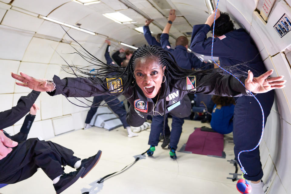 a woman floats at the front of a large group during a parabolic flight in an airplane