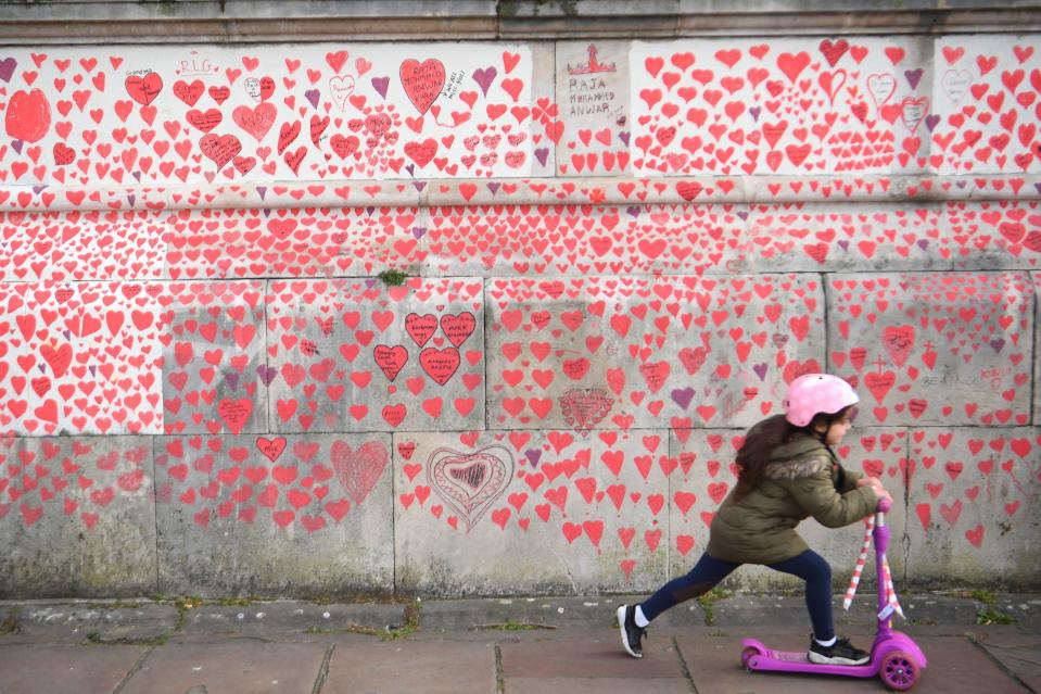 <p>A young girl rides a scooter past the National Covid Memorial Wall on the Embankment in London.</p> (PA)