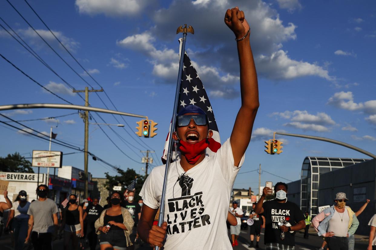 A protester carrying a U.S. flag leads a chant during a Black Lives Matter march through a residential neighborhood calling for racial justice, Monday, July 13, 2020, in Valley Stream, N.Y. 