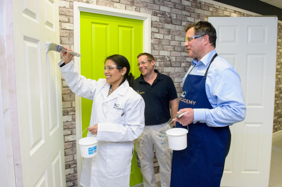 EDITORIAL USE ONLY Minister for Employment Priti Patel tries her hand at painting with Matt Gray, Painting Skills Development Manager and Matt Pullen, CEO of AkzoNobel, as she officially opens AkzoNobel's Dulux Academy, the UK's first training facility dedicated to painters and decorators, Slough, Surrey.