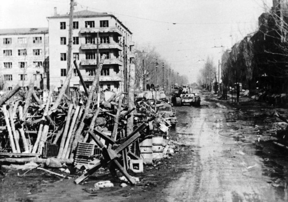Black-and-white image of tanks on an urban road strewn with debris.