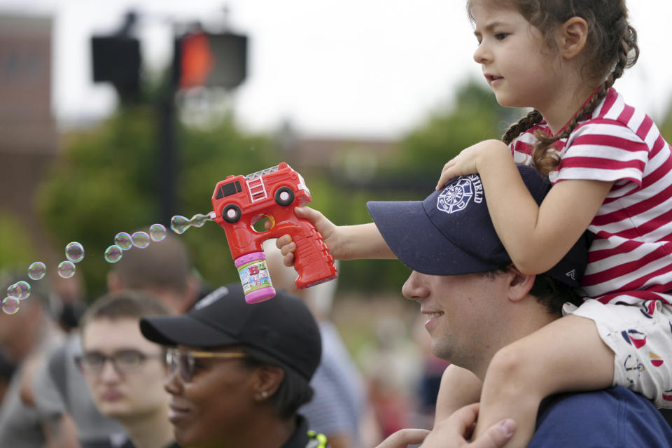 Madeline Couper, four years old, blows bubbles on the Fourth of July parade while sitting on her father, firefighter Jon Cooper's shoulders, Tuesday, July 4, 2023, in Pittsfield, Ma.. (Ben Garver/The Berkshire Eagle via AP)