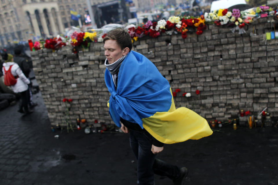 A youth draped in Ukraine's flag passes by a memorial to protesters killed in clashes with the police at Independence Square in Kiev, Ukraine, Sunday, Feb. 23, 2014. The Kiev protest camp at the center of the anti-President Viktor Yanukovych movement filled with more and more dedicated demonstrators Sunday morning setting up new tents after a day that saw a stunning reversal of fortune in a political standoff that has left scores dead and worried the United States, Europe and Russia. (AP Photo/ Marko Drobnjakovic)