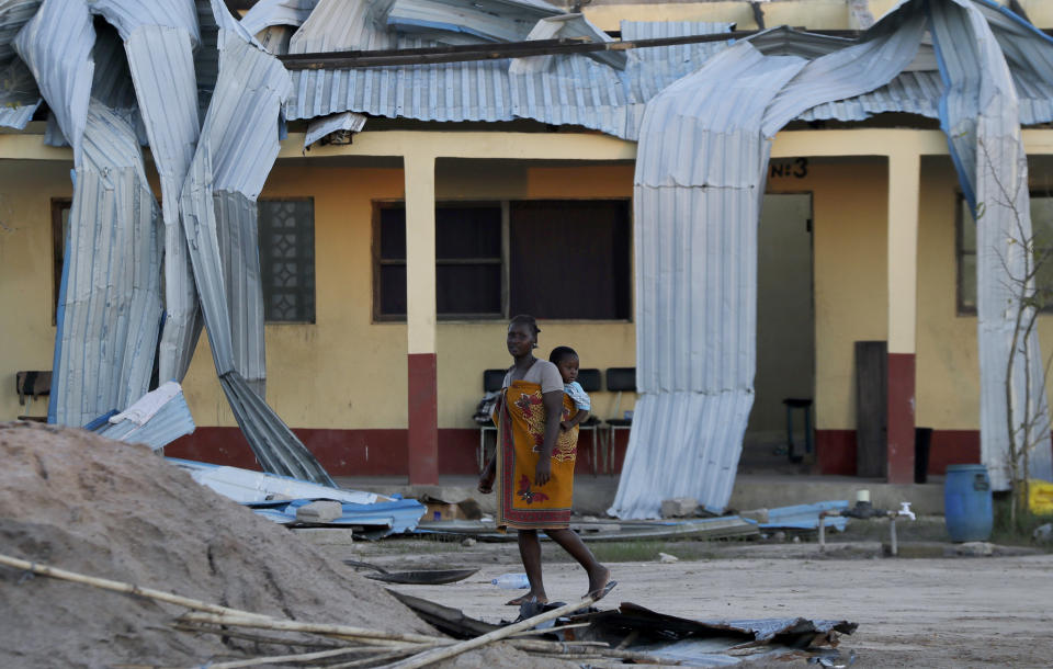 A woman carrying a baby on her back walks past damaged school in Beira, Mozambique, Monday, March 25, 2019. The United Nations is making an emergency appeal for $282 million for the next three months to help Mozambique start recovering from the devastation of Cyclone Idai. (AP Photo/Themba Hadebe)