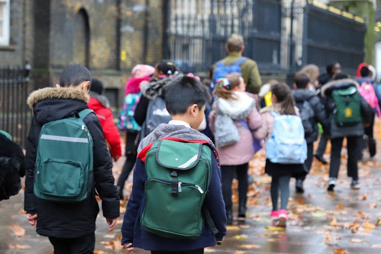 View from behind of a group of primary school children walking down a rainy street