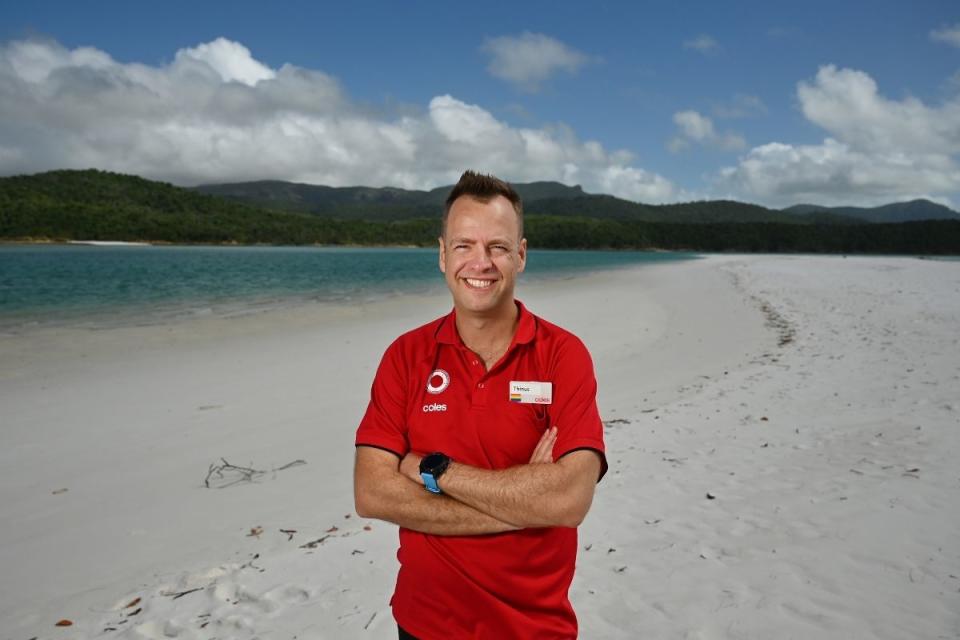 Thinus Keeve in red shirt, standing with arms crossed, smiling, on tropical beach