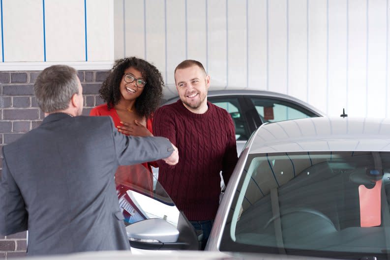 Couple shakes hand with a car salesman near a vehicle for sale.