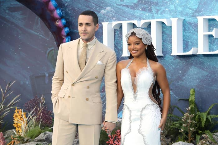 Jonah Hauer-King and Halle Bailey hold hands as they pose for photographers at the premiere of The Little Mermaid