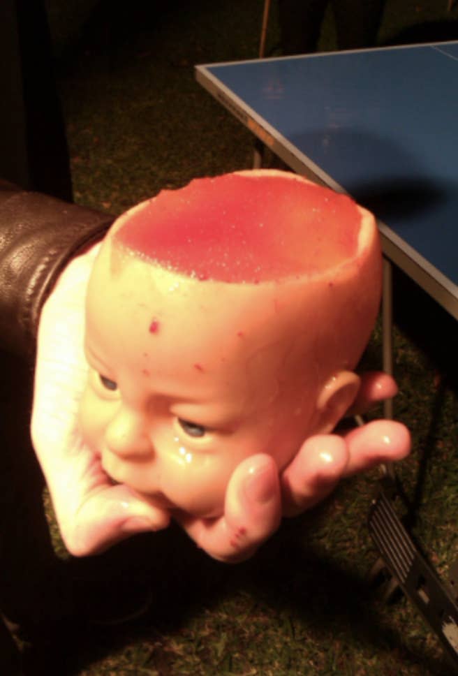 A drink in a mug in the shape of a baby doll's head with the top of the head missing