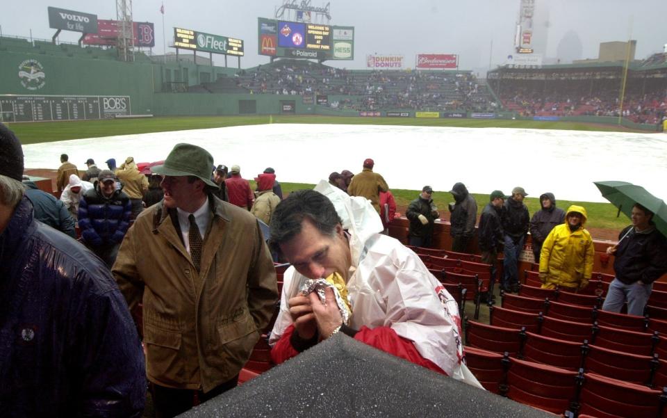 BOSTON - APRIL 11, 2003: Gov. Mitt Romney tries to get a bite in the rain at his seat near the third base line, on what was going to be opening day - until the Red Sox were rained out. (Photo by Michele McDonald/The Boston Globe via Getty Images)