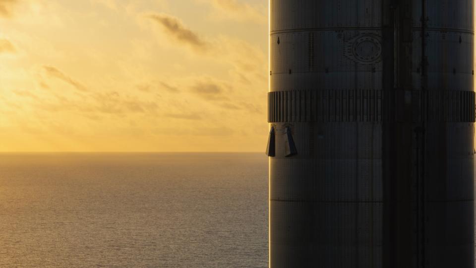 closeup of the side of a silver rocket booster, with the sun setting over the ocean in the background