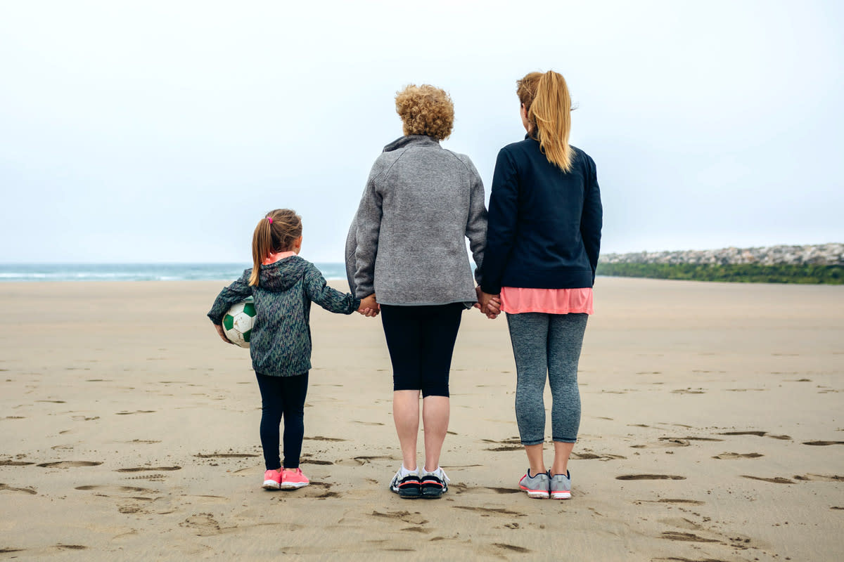 Three generations look out at the water while holding hands. 