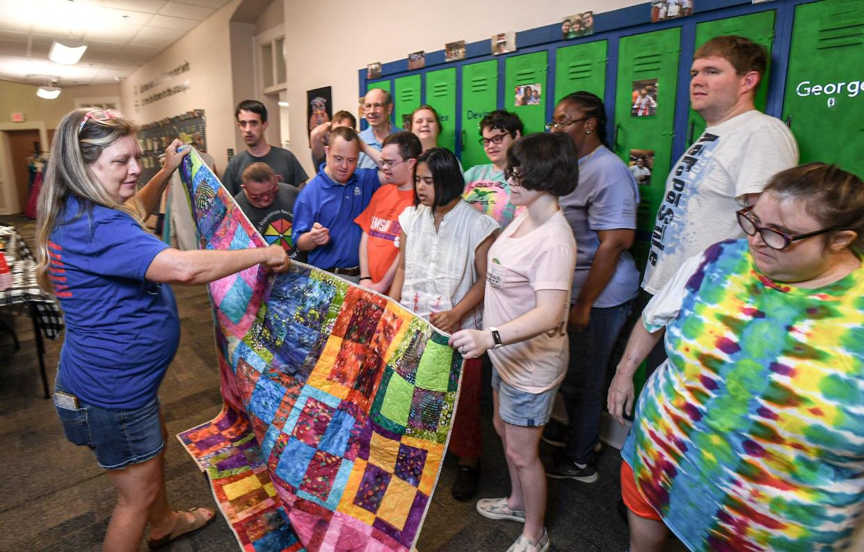 Kim Price gives members of the Rainbow Gang Special Population day care a quilt presented by the Quilts of Valor Foundation in Anderson, S.C., Monday, August 12, 2024. The group made colorful squares as an art project, which Kim Price secretly made into a quilt which she surprised them, and posed for a group photo with.