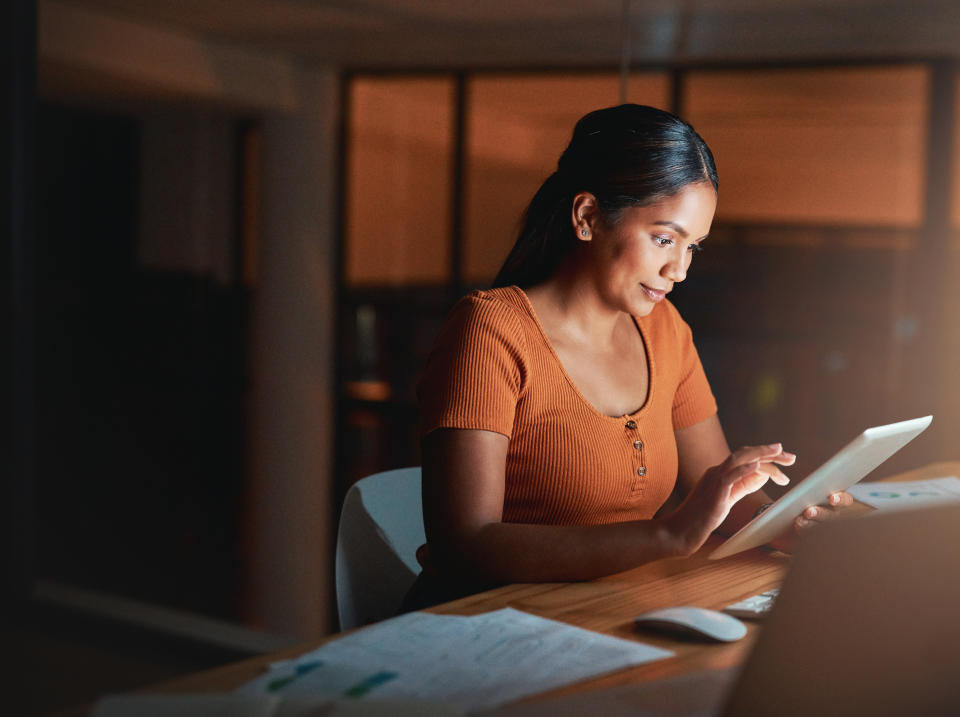 Indian woman looking at a tablet while working in her home office late at night, and reviewing her investment portfolio