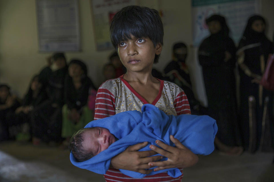 FILE - In this Sept. 13, 2017, file photo, Rohingya Muslim girl Afeefa Bebi, who crossed over from Myanmar into Bangladesh holds her few-hours-old brother as doctors check her mother Yasmeen Ara at a community hospital in Kutupalong refugee camp, Bangladesh. A new report by the United Nations children’s agency says the lives and futures of more than 19 million Bangladeshi children are at risk from colossal impacts of devastating floods, cyclones and other environmental disasters linked to climate change. The UNICEF report released Friday, April 5, 2019 said the tally includes Rohingya refugee children from Myanmar who are living in squalid camps in southern Bangladesh. (AP Photo/Dar Yasin, File)