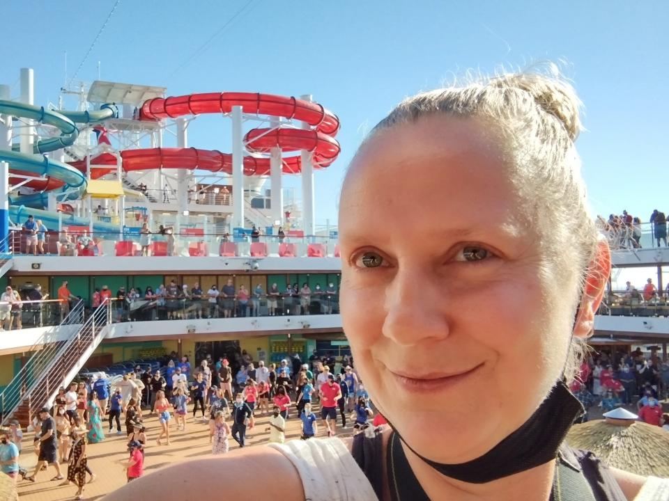 A woman with a mask under her chin takes a selfie in front of a cruise ship waterslide.