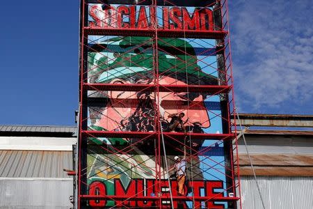 Men paint an image depicting Cuba's former President Fidel Castro with a writing that reads "Socialism or Death", Havana, Cuba, August 11, 2016. REUTERS/Stringer