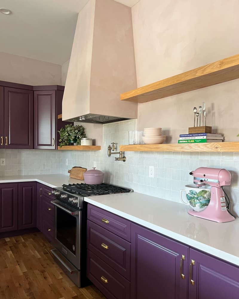 Pink kitchenaid on countertop in kitchen with pink painted walls and eggplant cabinets.