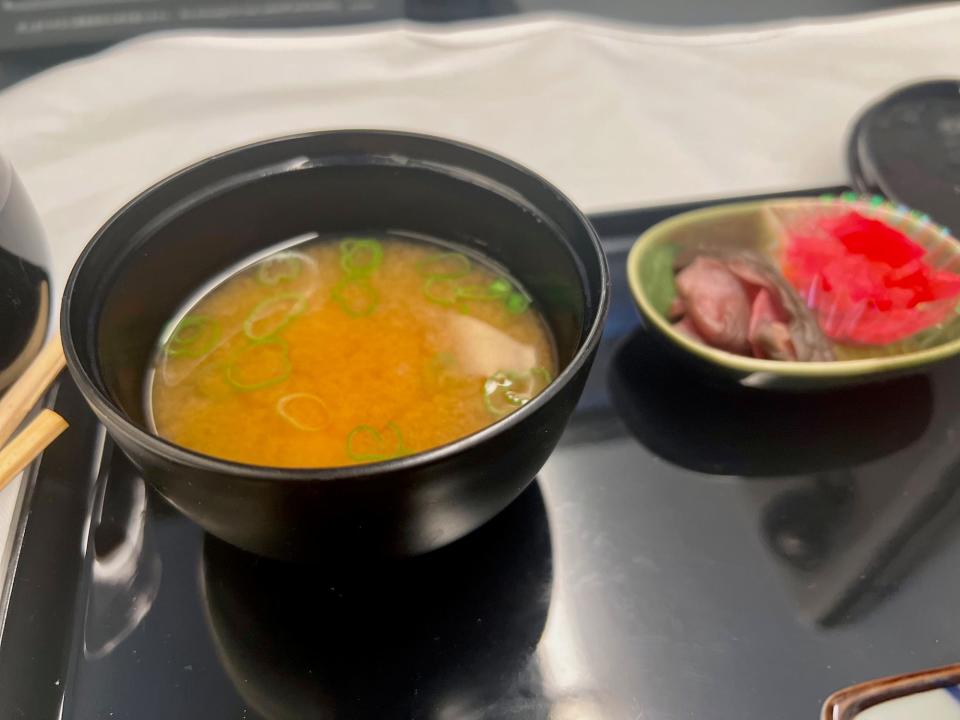 A tray of airline food, including a small bowl of miso soup.