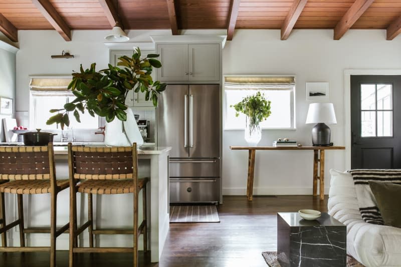 Red wood ceiling with large beams, dark front door, small peninsula island, with tall woven back bar stools