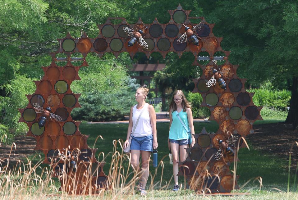 Visitors look at the More Bees Please! sculpture in the "Glass in Flight" exhibition by Alex Heveri at Reiman Gardens.