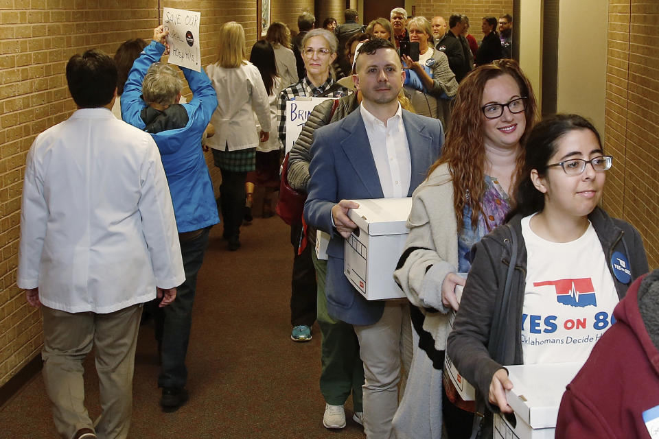 FILE - In this Oct. 24, 2019, file photo, supporters of Yes on 802 Oklahomans Decide Healthcare, calling for Medicaid expansion to be put on the ballot, carry boxes of petitions into the office of the Oklahoma Secretary of State in Oklahoma City. Oklahoma voters will decide Tuesday, June 30, 2020, whether to expand Medicaid to tens of thousands of low-income residents and become the first state to amend their Constitution to do so. (AP Photo/Sue Ogrocki, File)