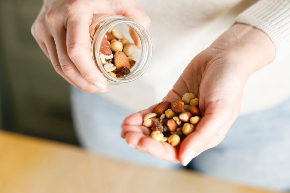 A woman pours a handful of nuts from a jar into her hand. 
