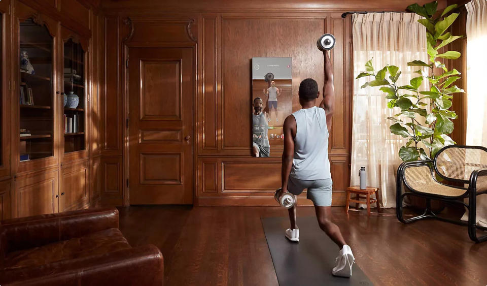 Man lifts weights in his living room while using the Mirror home gym