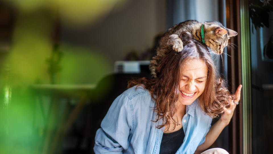 Woman laughing happily with a cat on her head