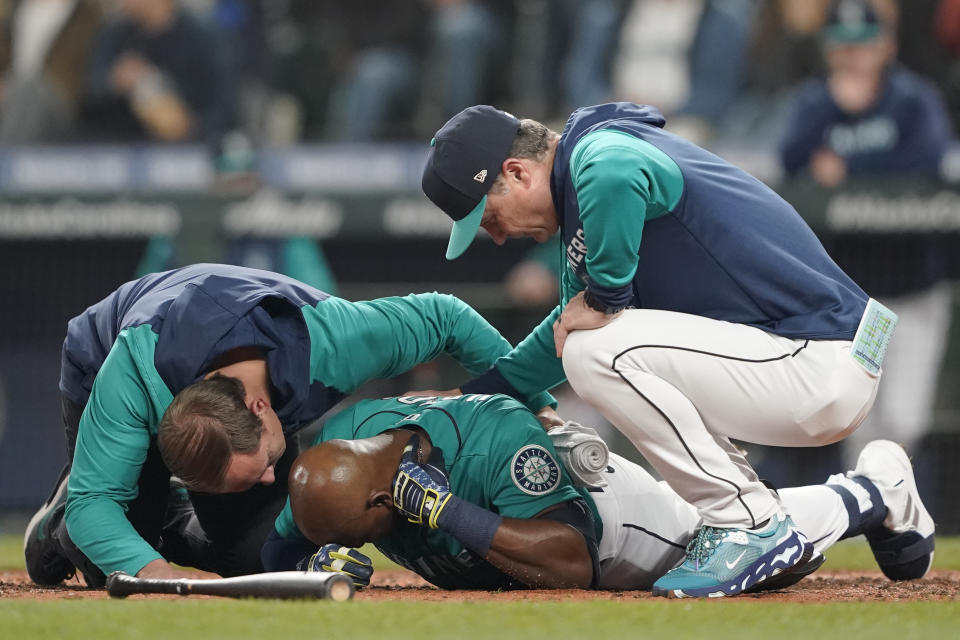 Seattle Mariners' Justin Upton, center, points to where he was hit by a pitch during the fifth inning of a baseball game against the Los Angeles Angels as he is examined by a trainer, left, and manager Scott Servais, right, Friday, June 17, 2022, in Seattle. Upton left the game after the injury. (AP Photo/Ted S. Warren)