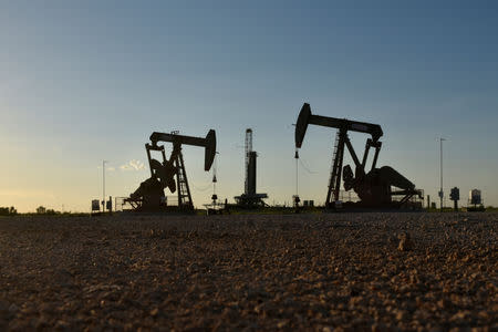 FILE PHOTO: Pump jacks operate in front of a drilling rig in an oil field in Midland, Texas U.S. August 22, 2018. REUTERS/Nick Oxford/File Photo/File Photo