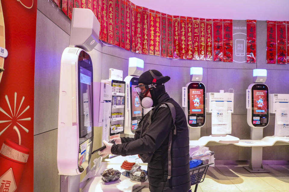 A shopper wearing goggles, a face mask and gloves uses a self checkout machine at a supermarket in Wuhan in central China's Hubei province, Saturday, Jan. 25, 2020. The virus-hit Chinese city of Wuhan, already on lockdown, banned most vehicle use downtown and Hong Kong said it would close schools for two weeks as authorities scrambled Saturday to stop the spread of an illness that is known to have infected more than 1,200 people and killed 41, according to officials. (Chinatopix via AP)