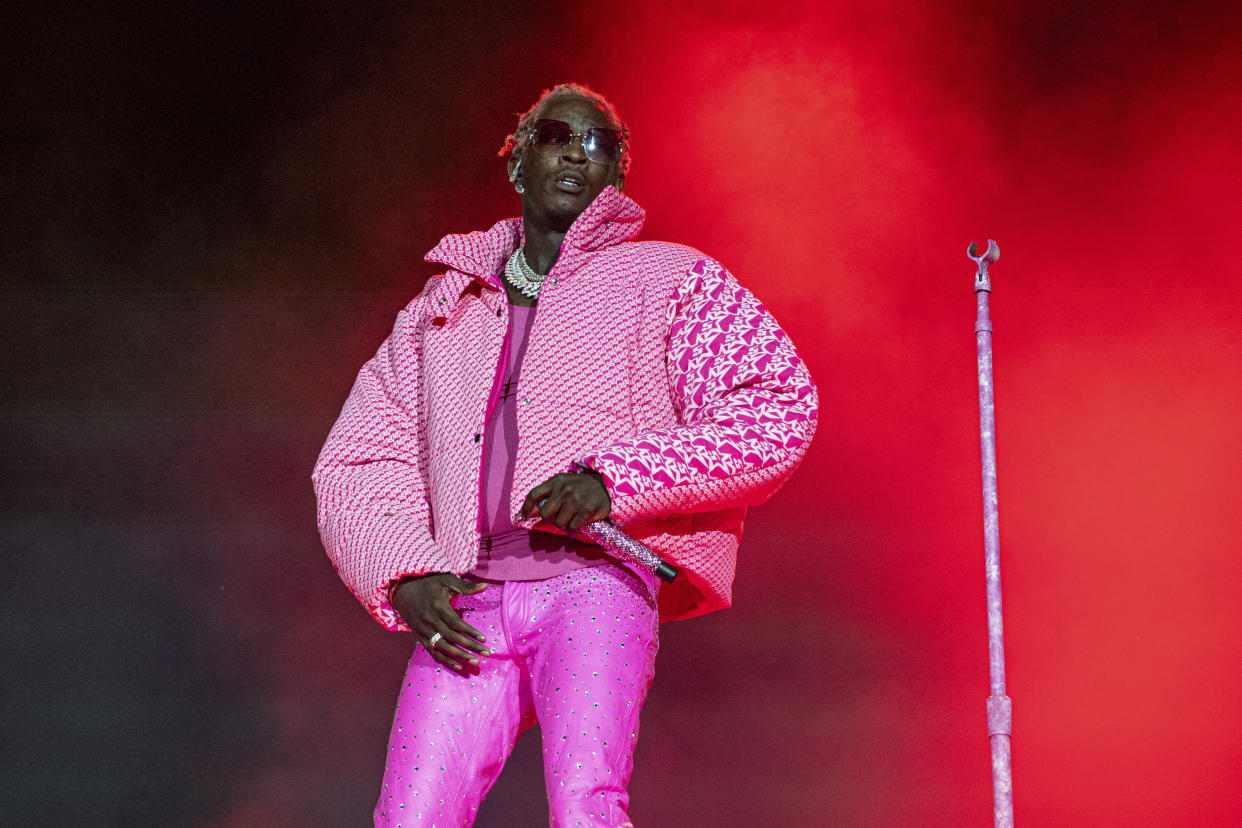 Young Thug onstage wearing dark glasses, a huge necklace, tight fuchsia pants dotted with glitter and a huge puffy jacket in a bright pink print.