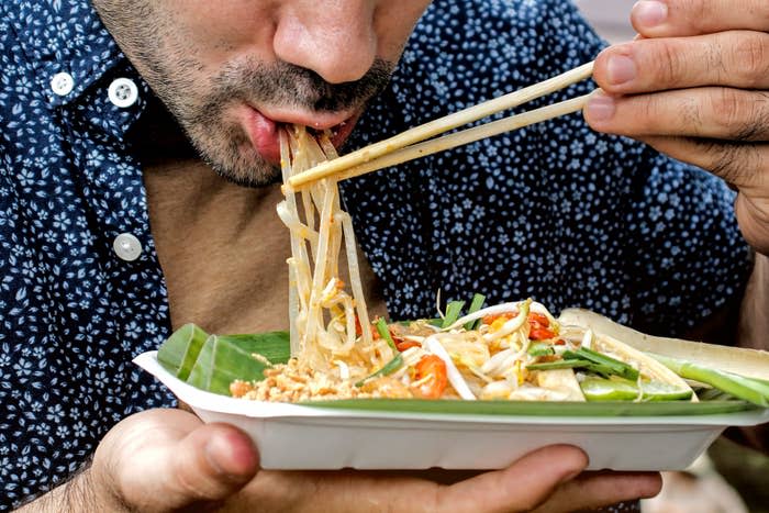 Person eating noodles from a takeout box, conveying enjoyment of local street food