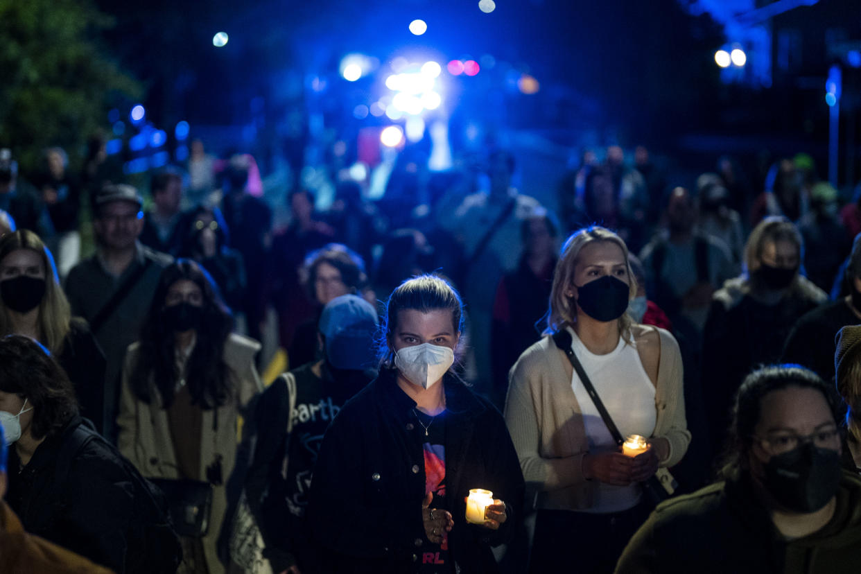 Two women in surgical masks, flanked by other protesters, stand in vigil holding candles in the dark.