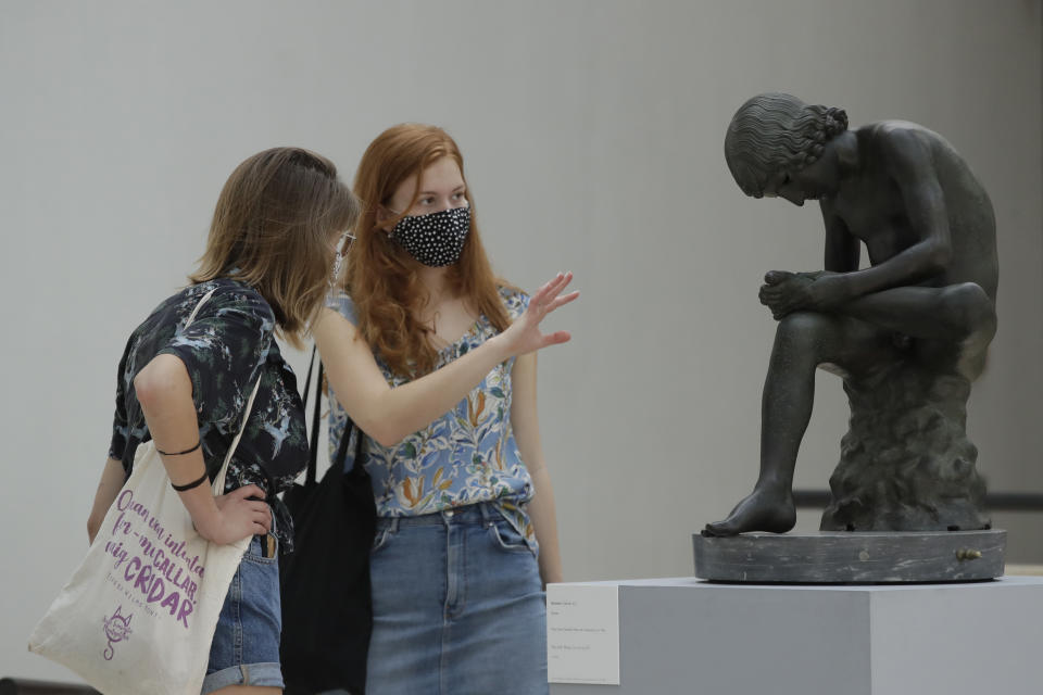 Visitors wearing face mask to prevent the spread of COVID-19, look at 'The Boy with Thorn" a first century B.C. bronze statue in the Rome's Capitoline Museums, Tuesday, May 19, 2020. In Italy, museums were allowed to reopen this week for the first time since early March, but few were able to receive visitors immediately as management continued working to implement social distancing and hygiene measures, as well as reservation systems to stagger visits to museums in the onetime epicenter of the European pandemic. (AP Photo/Alessandra Tarantino)