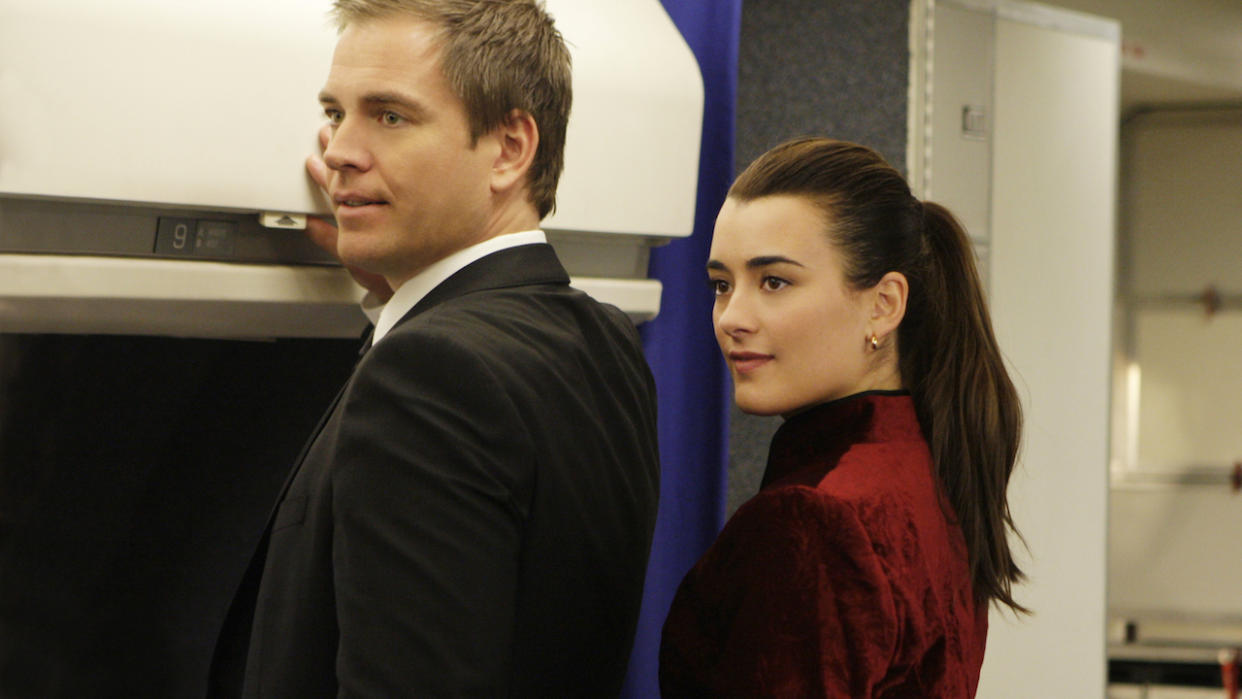  Michael Weatherly and Cote de Pablo near overhead luggage compartment aboard plane. 