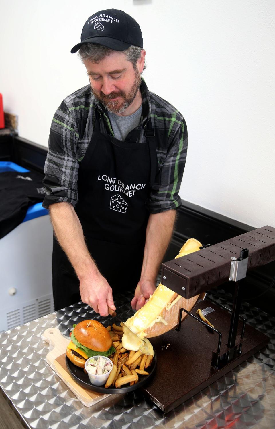 Long Branch Gourmet owner David Enright scrapes Raclette cheese onto fries at the Ocean Avenue North shop Tuesday, November 8, 2022.  The shop opened earlier this year and features cheese & charcuterie; deli and specialty foods store.